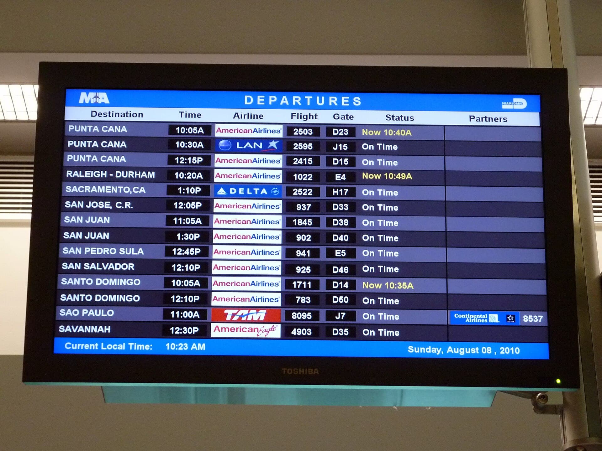 An airport departures board listing flights to Punta Cana, San Juan and Santo Domingo at Miami