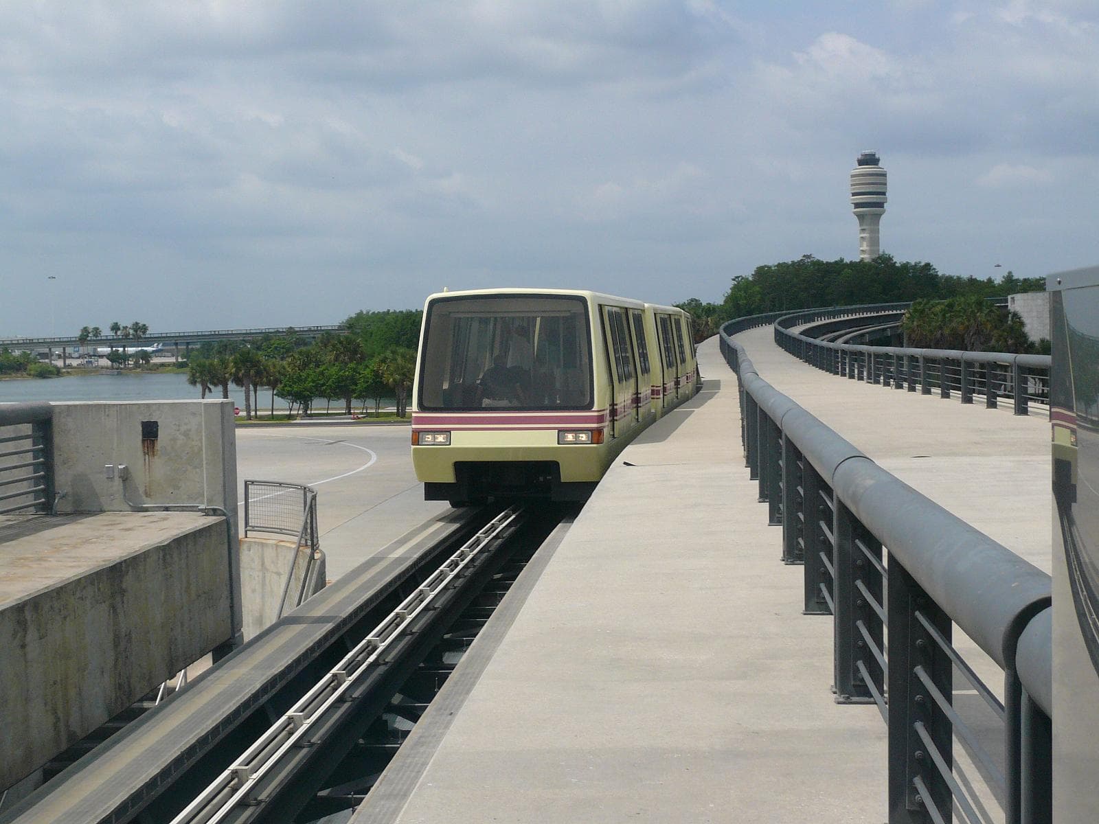 Orlando airport people mover shuttle arriving on its elevated track, the control tower in the distance
